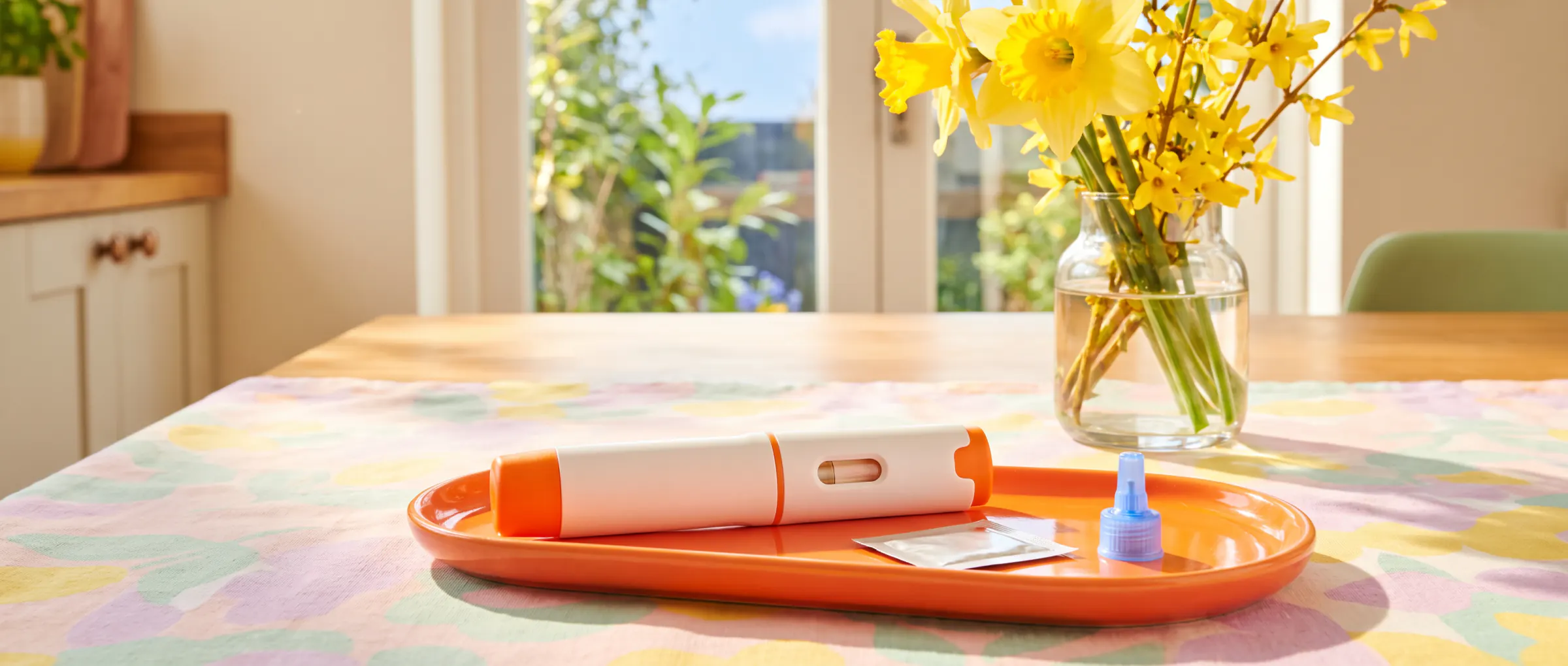An injection pen and a swab laid out on a colourful tray in a sunny kitchen
