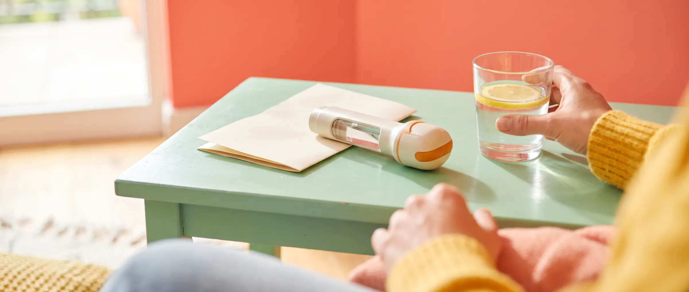 A folded leaflet beside an injection pen on a sunny mint-green table